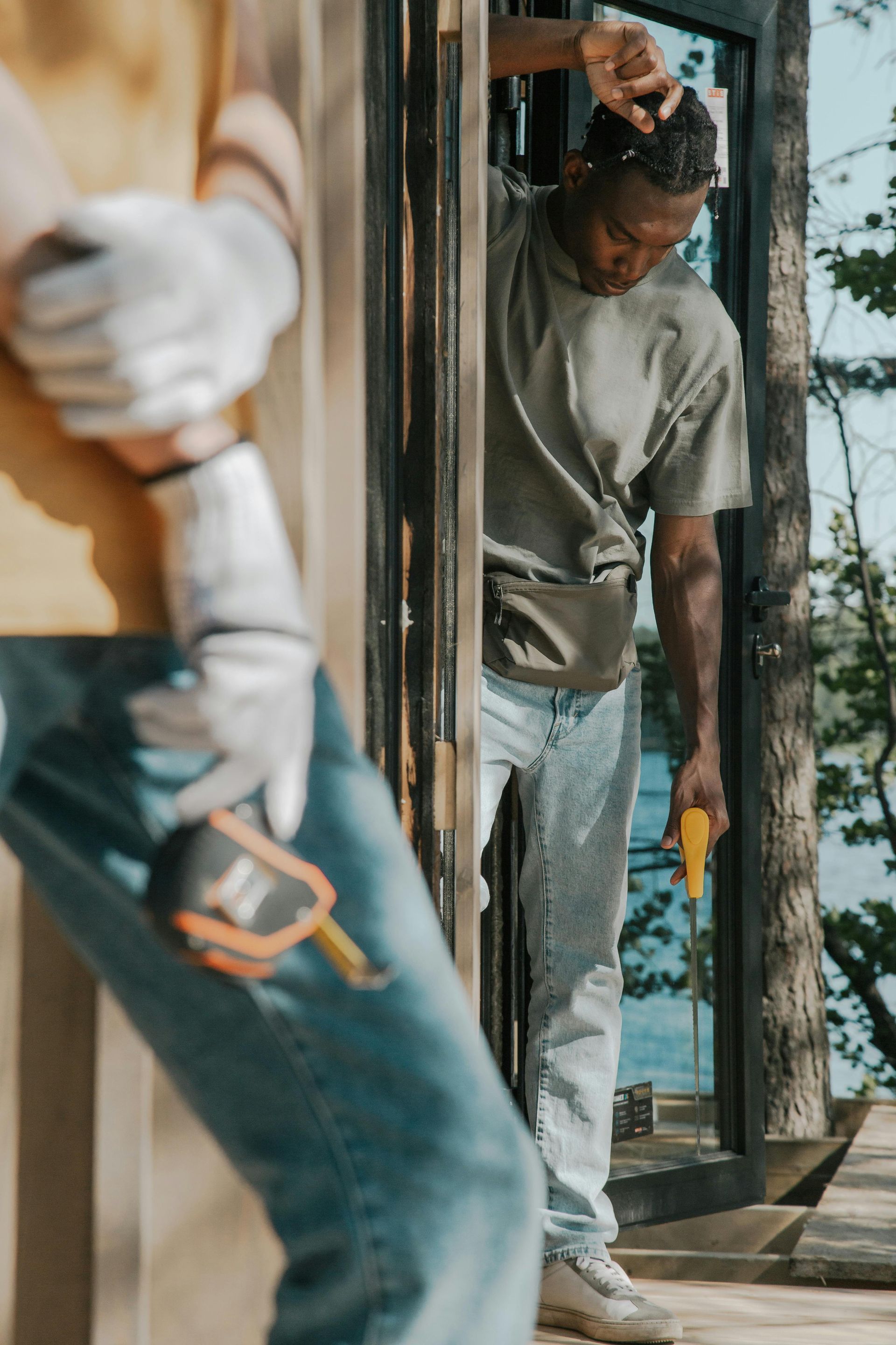 Worker standing in a doorway with a yellow tool, with another person blurred in the foreground