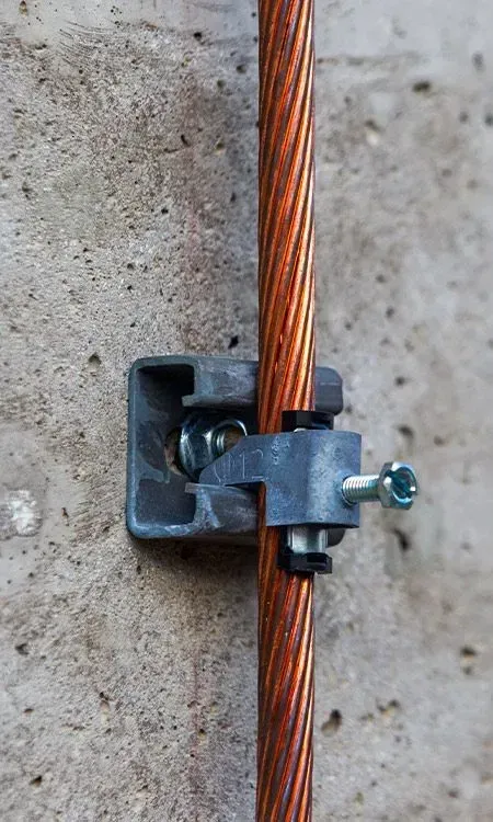 Copper grounding wire held to a concrete wall with a gray clamp and screw.