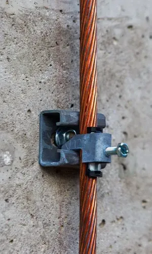 Copper grounding wire held to a concrete wall with a gray clamp and screw.