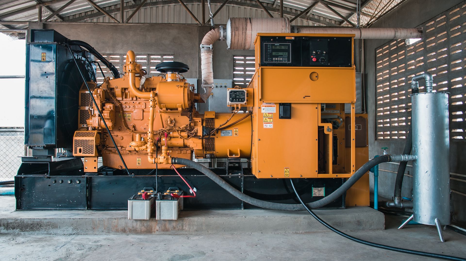 Yellow industrial generator in a concrete enclosure; electrical cables and equipment visible.