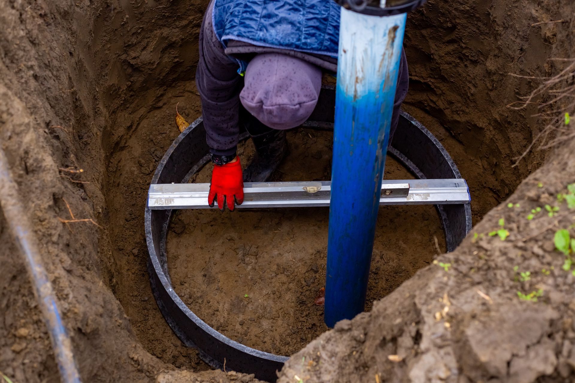 Person installing a black pipe ring inside a circular hole in the ground, using a level.