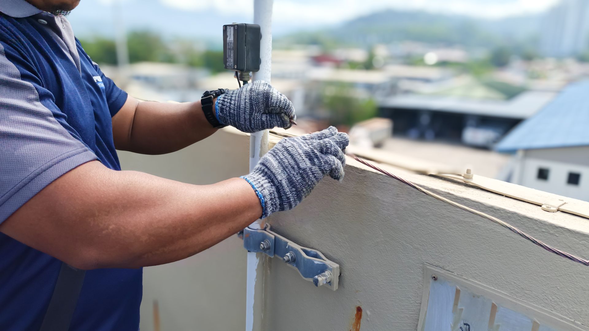 Man in gloves using a tool to work on a rooftop, outdoors.