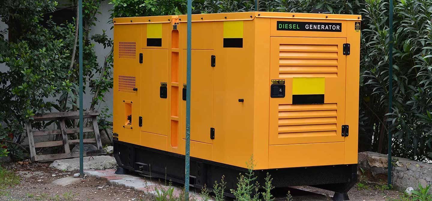 Yellow generator in a grassy area surrounded by bushes.