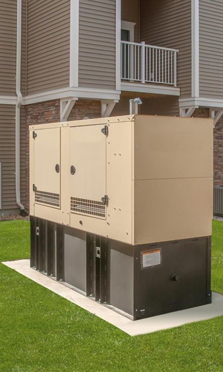 Tan and black generator box on a concrete pad, outside a building with beige siding and a balcony.