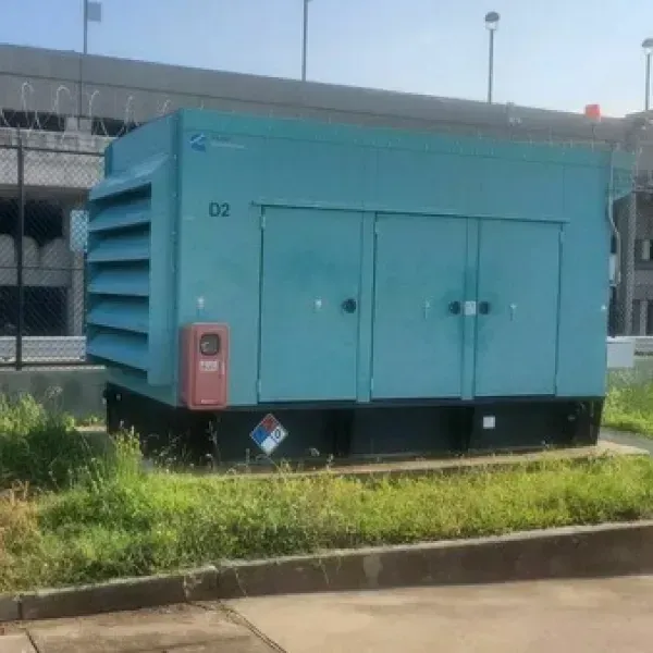 Light blue generator with vent on left, two doors in front, and a red box on the side, outdoors.