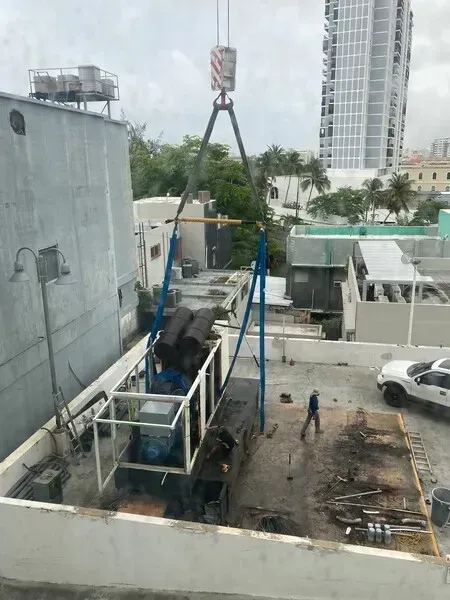 Crane lifting an industrial unit onto a rooftop, workers nearby.