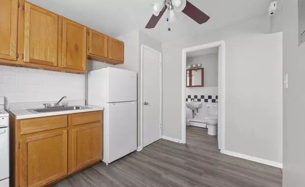 A kitchen with wooden cabinets , a refrigerator , a sink , and a ceiling fan.