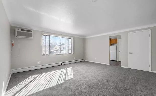 An empty living room with a large window and a gray carpet.