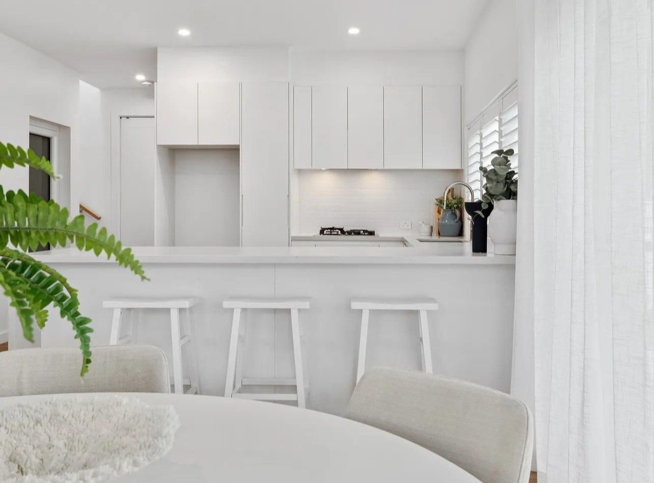 A Kitchen With White Cabinets, Stools, a Table and a Plant — JMB Electrical Services In Wollongong, NSW