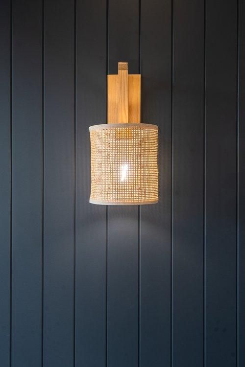 A Wall Light With a Wicker Shade is Hanging on a Dark Wooden Wall — JMB Electrical Services In Port Kembla, NSW