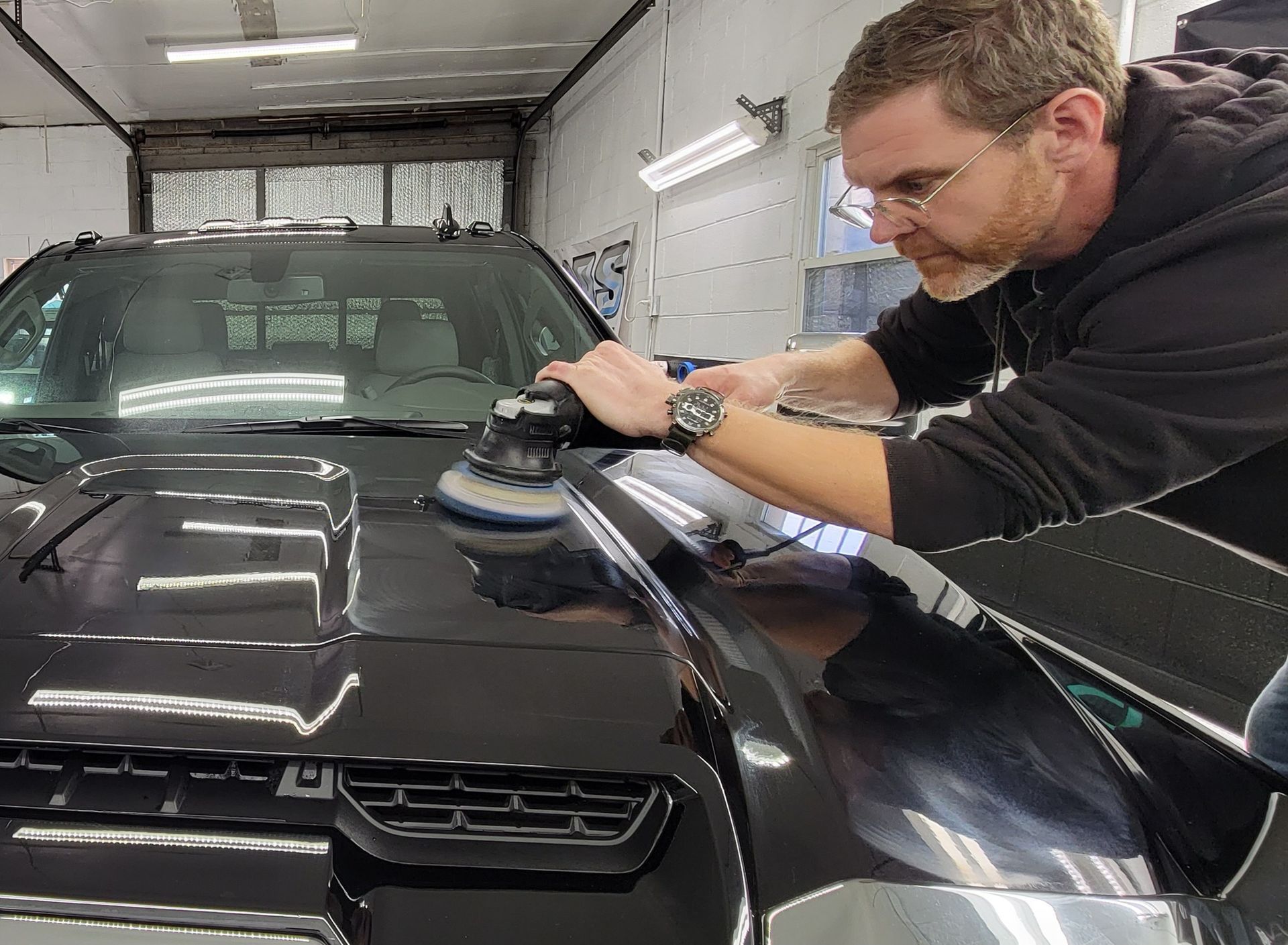 A man is polishing the hood of a black car