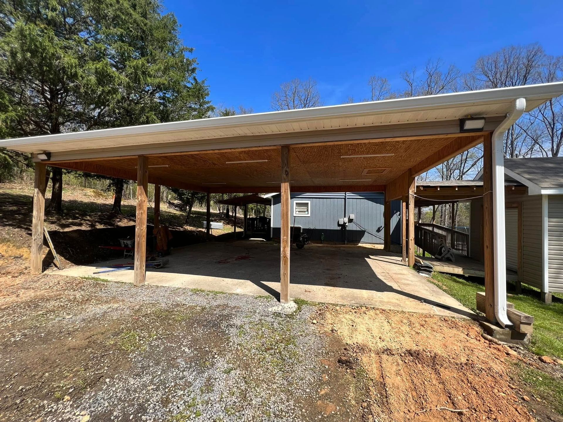 A wooden carport with a metal roof and a trailer parked underneath it.
