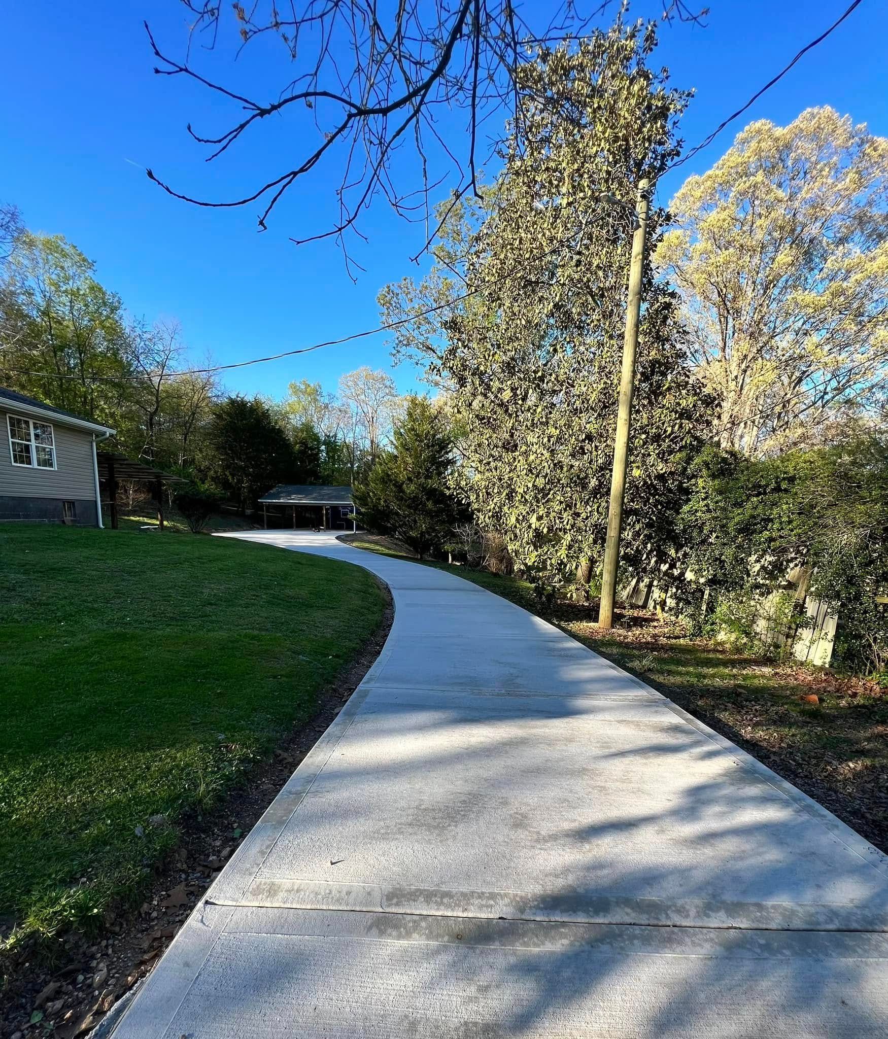 A concrete walkway leading to a house with trees on both sides.