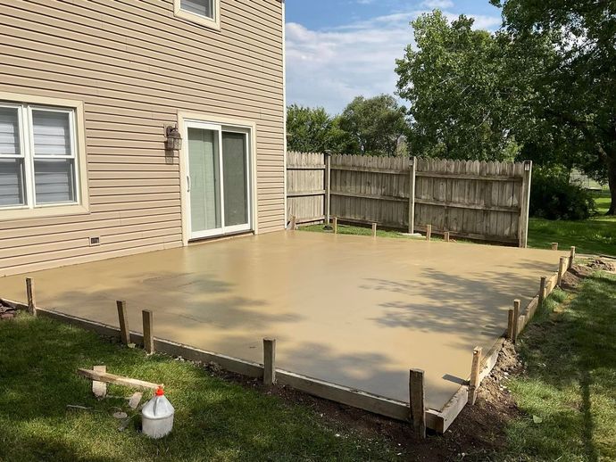A concrete patio is being built in the backyard of a house.