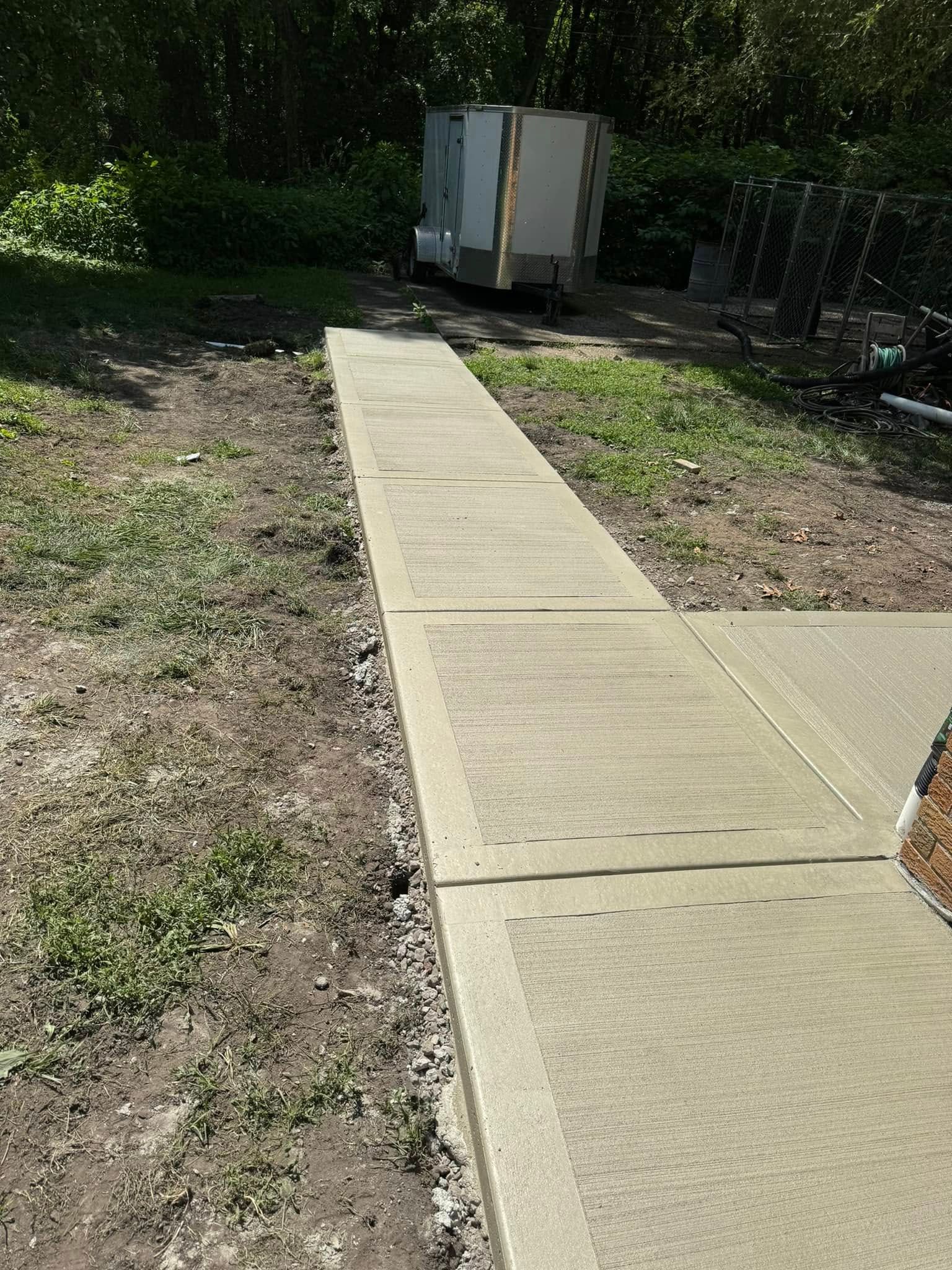 A concrete walkway is being built in a yard next to a trailer.