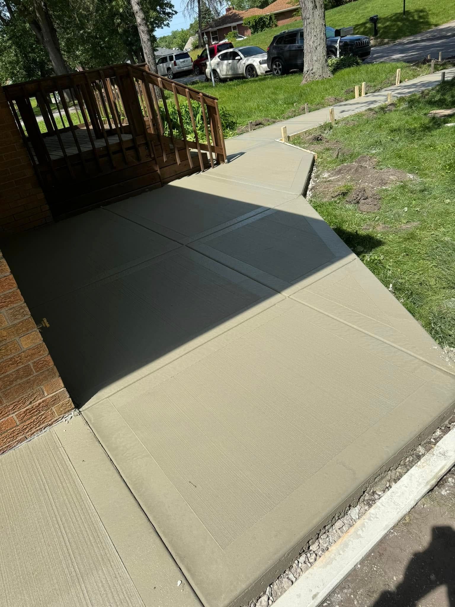 A concrete walkway leading to a house with a wooden deck.
