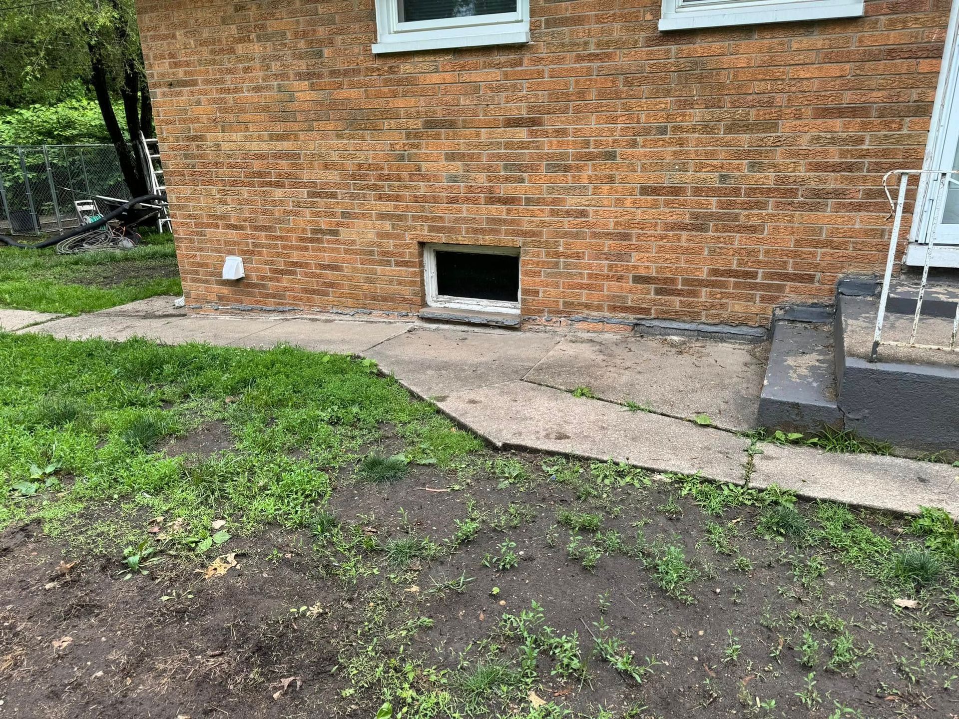 A brick house with a window and a sidewalk in front of it.