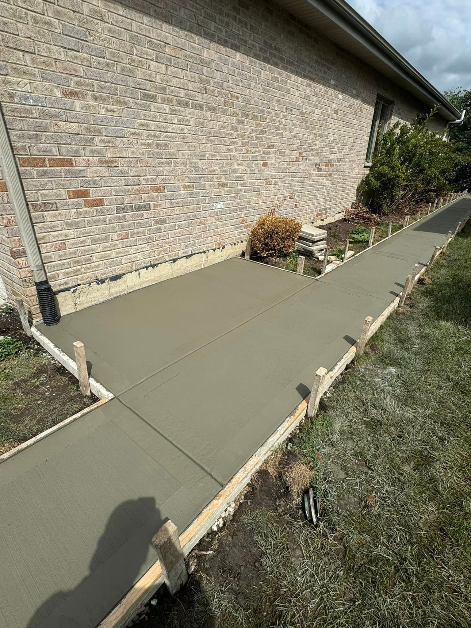 A concrete walkway is being built in front of a brick house.