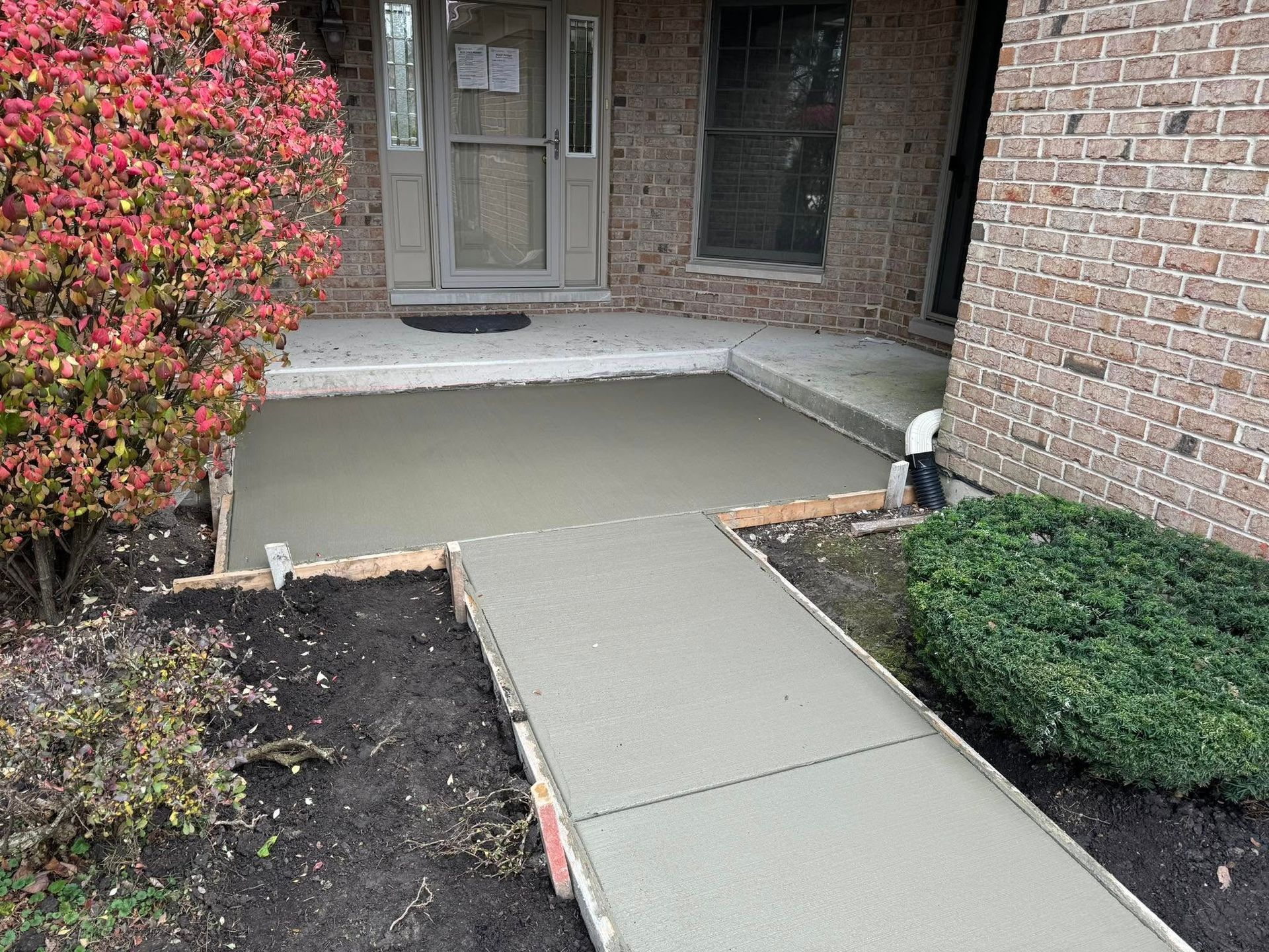 A concrete walkway is being built in front of a brick house.