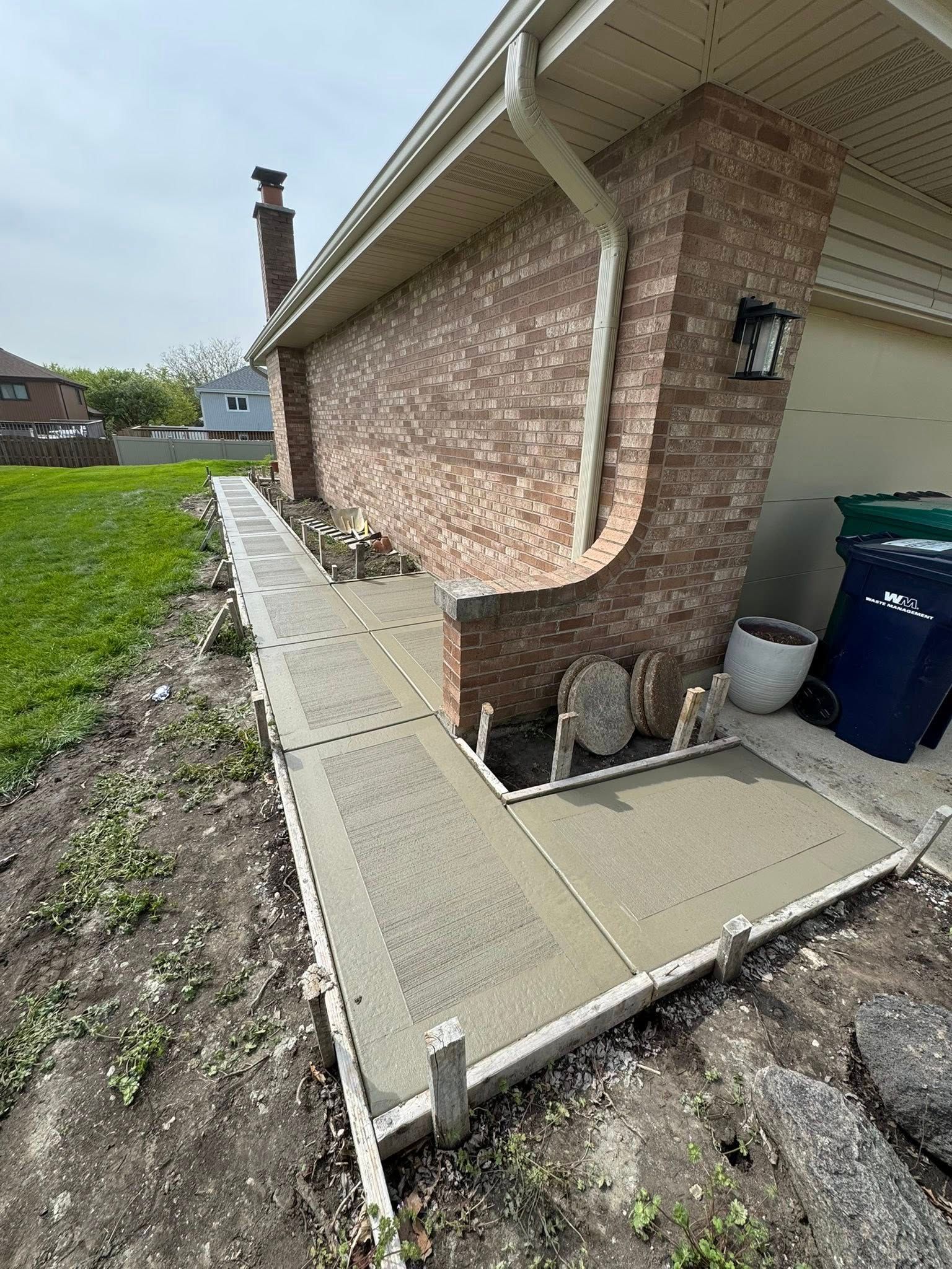A concrete walkway is being built in front of a brick house.