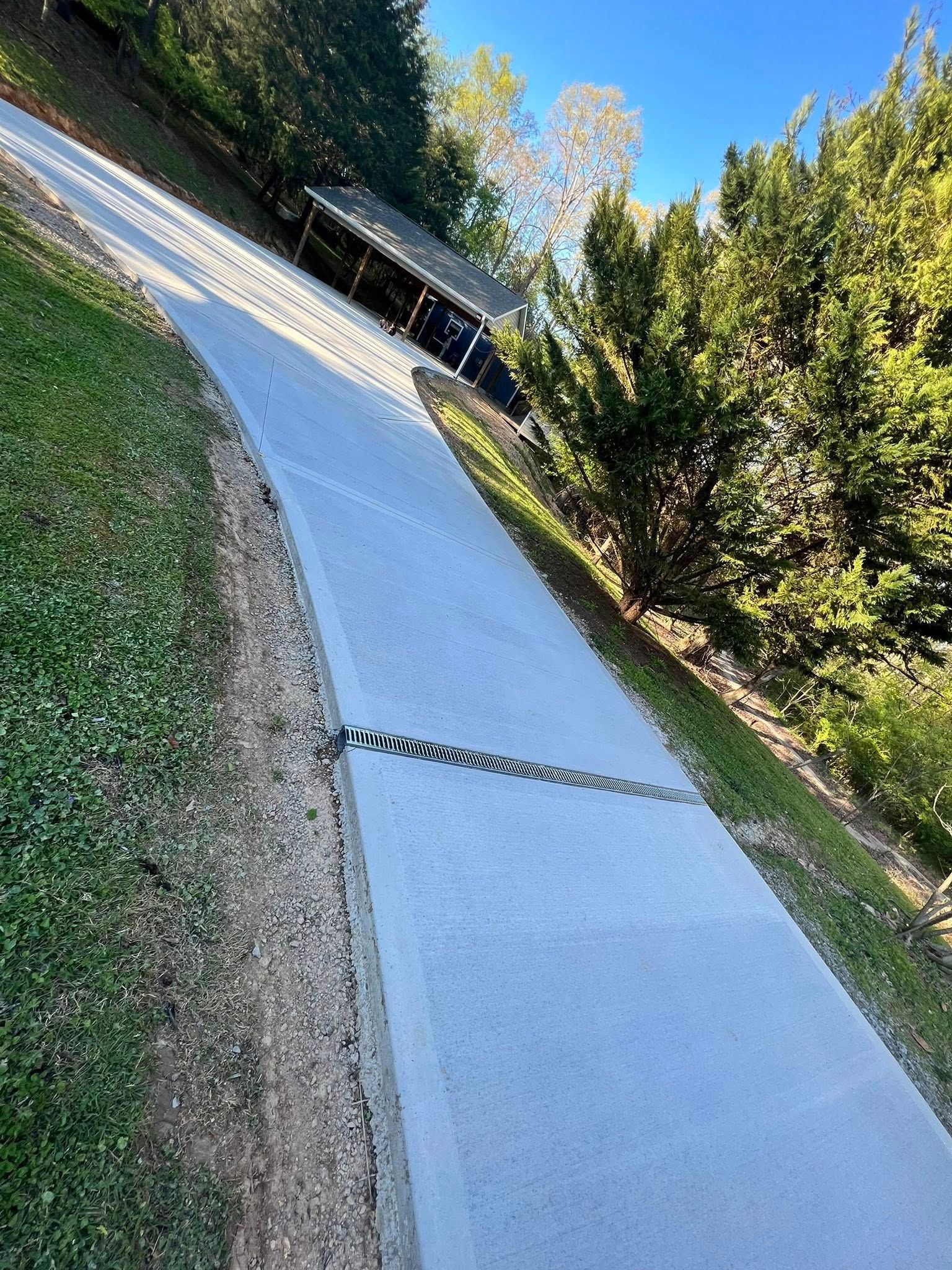 A concrete driveway going up a hill next to a house.