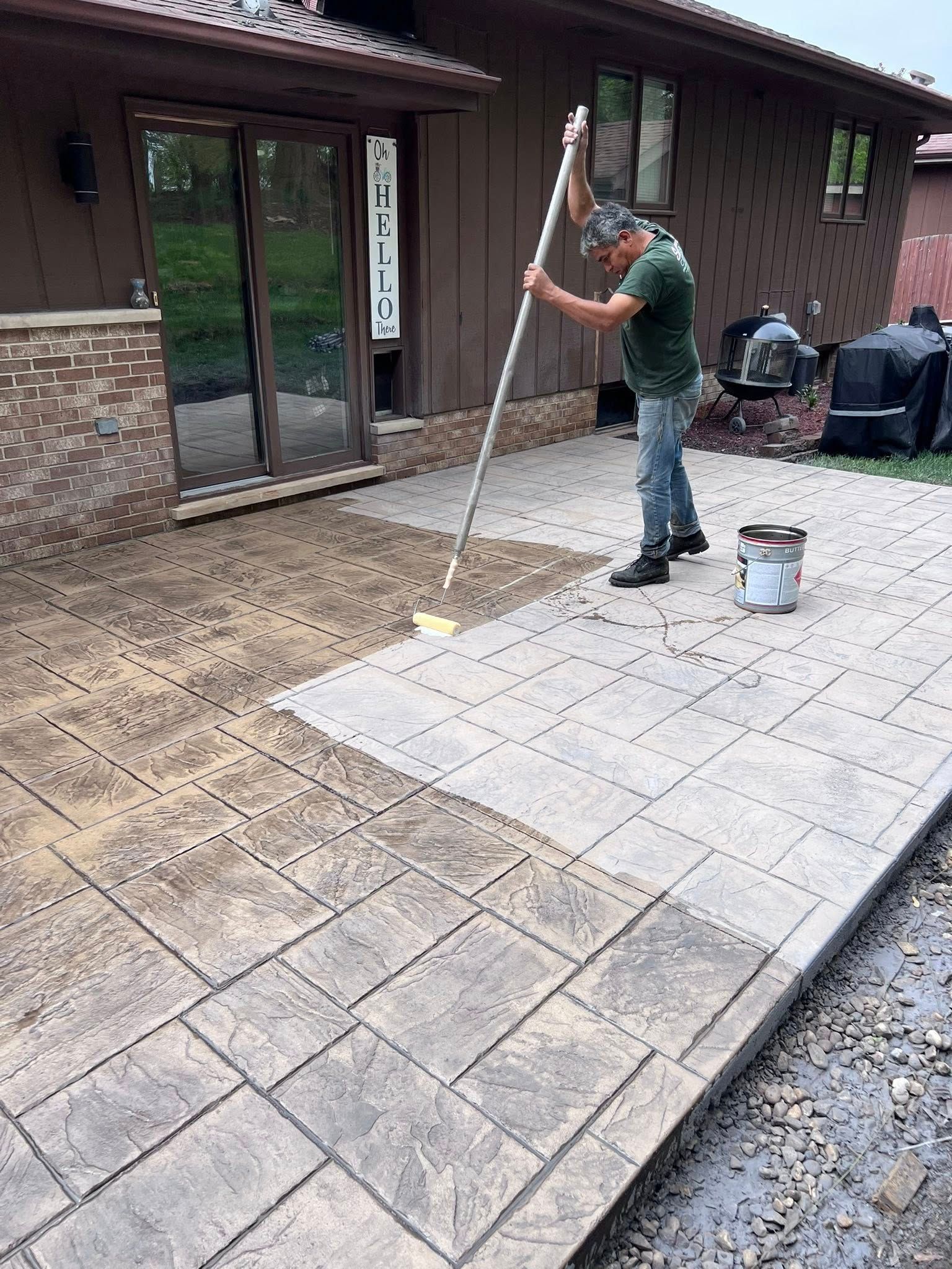 A man is painting a concrete patio in front of a house.