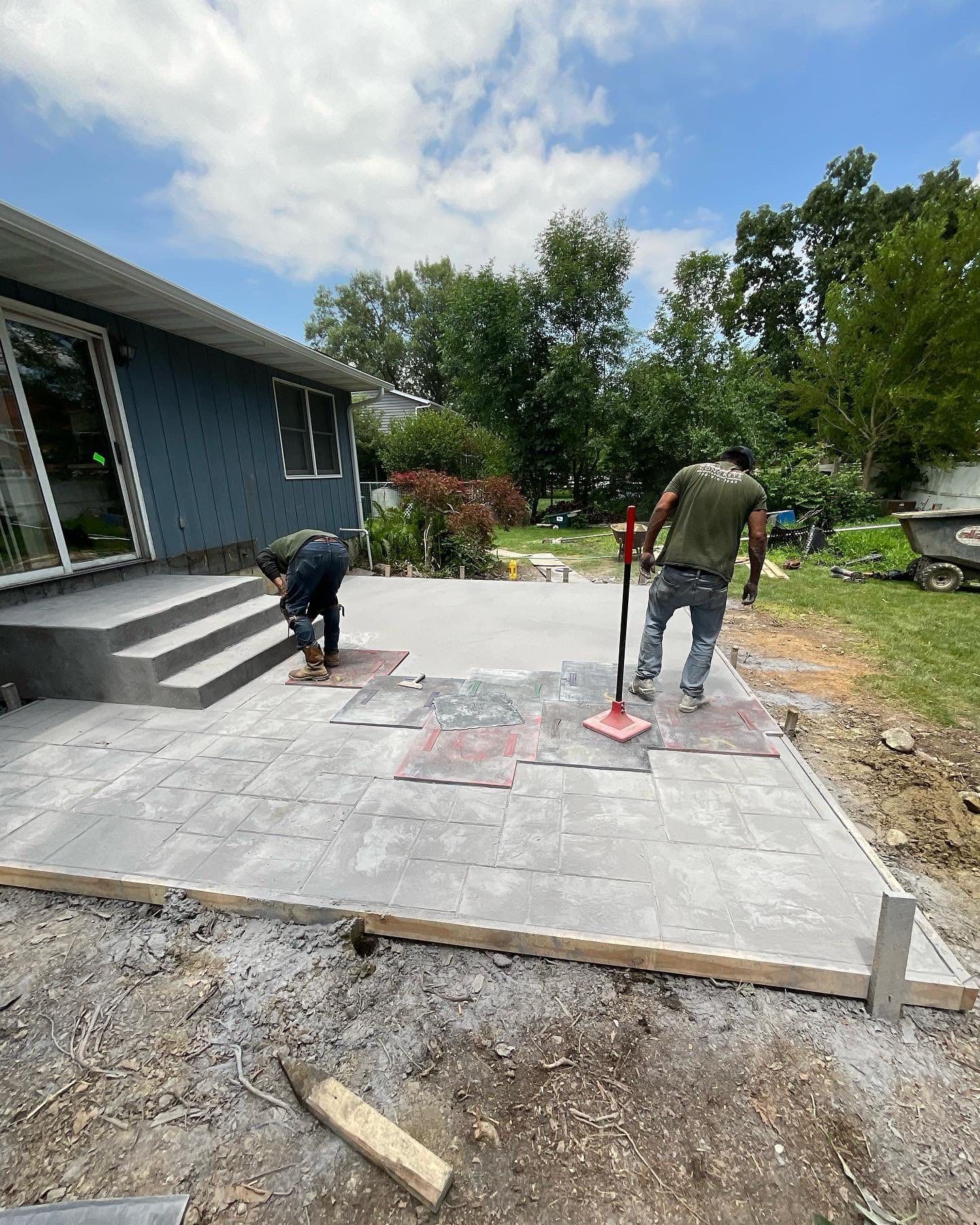 Two men are working on a patio in front of a house.
