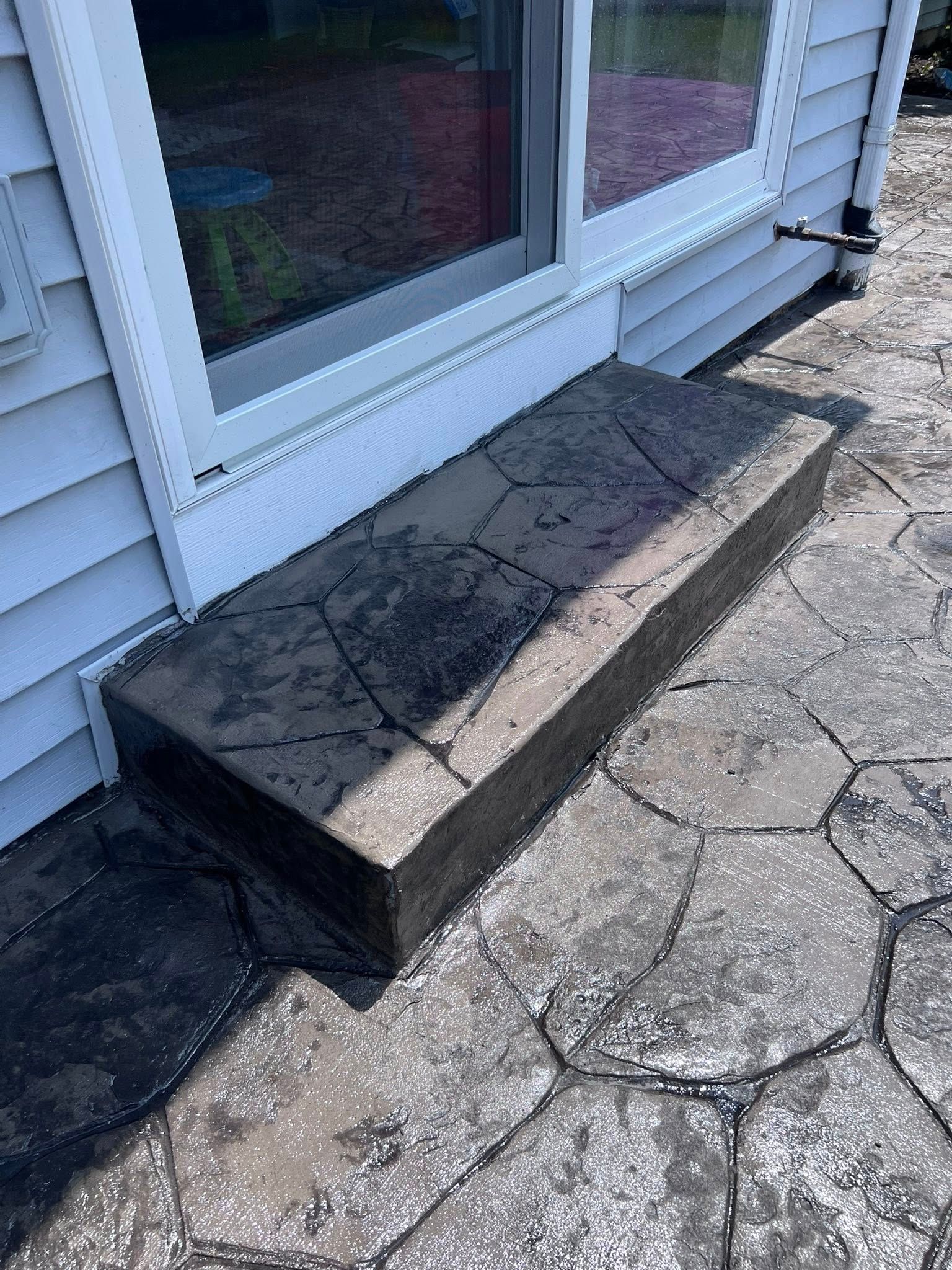 A concrete step next to a window on a patio next to a house.
