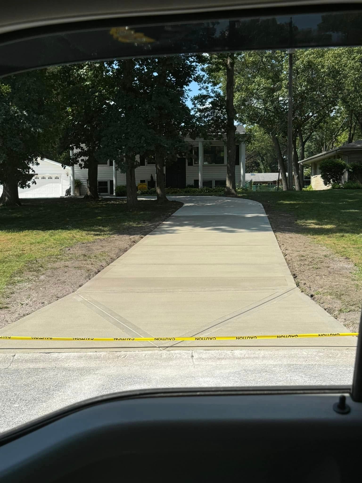 A car is driving down a concrete driveway towards a house.