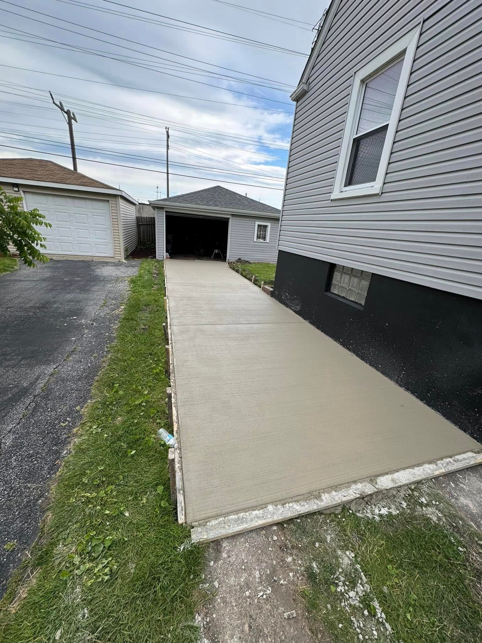 A concrete walkway leading to a garage next to a house.