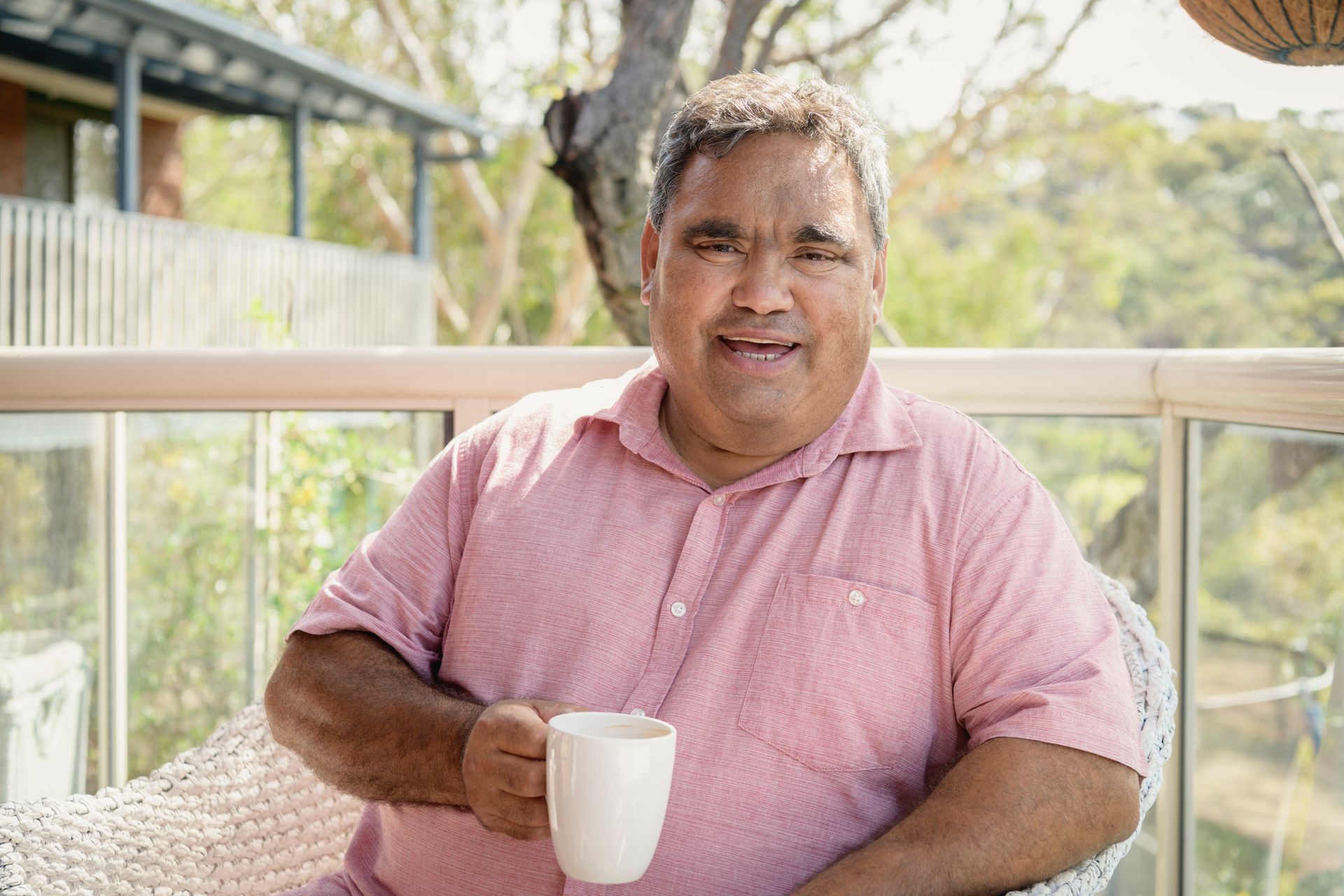 A man is sitting on a balcony holding a cup of coffee.