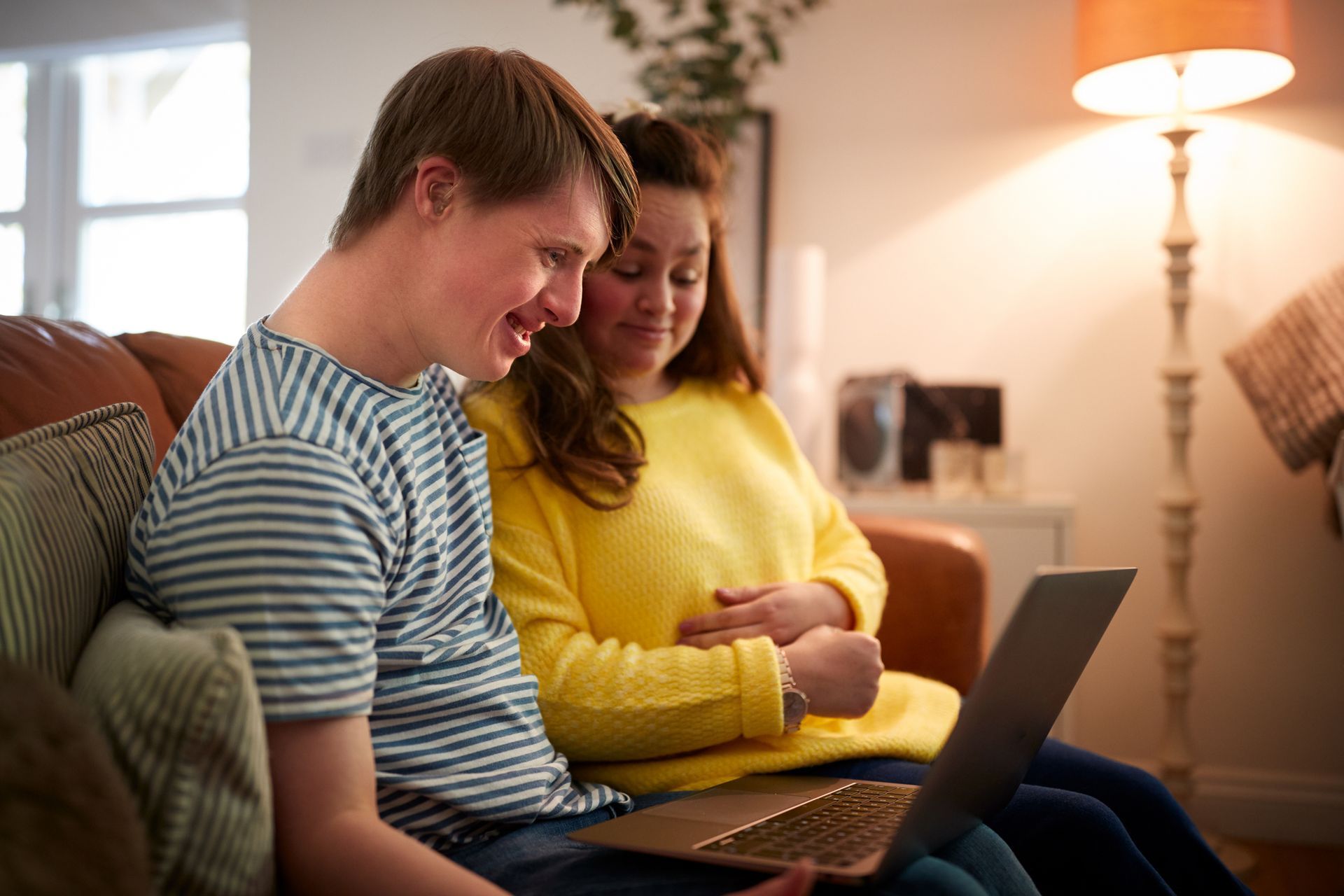 A man and a woman are sitting on a couch looking at a laptop.