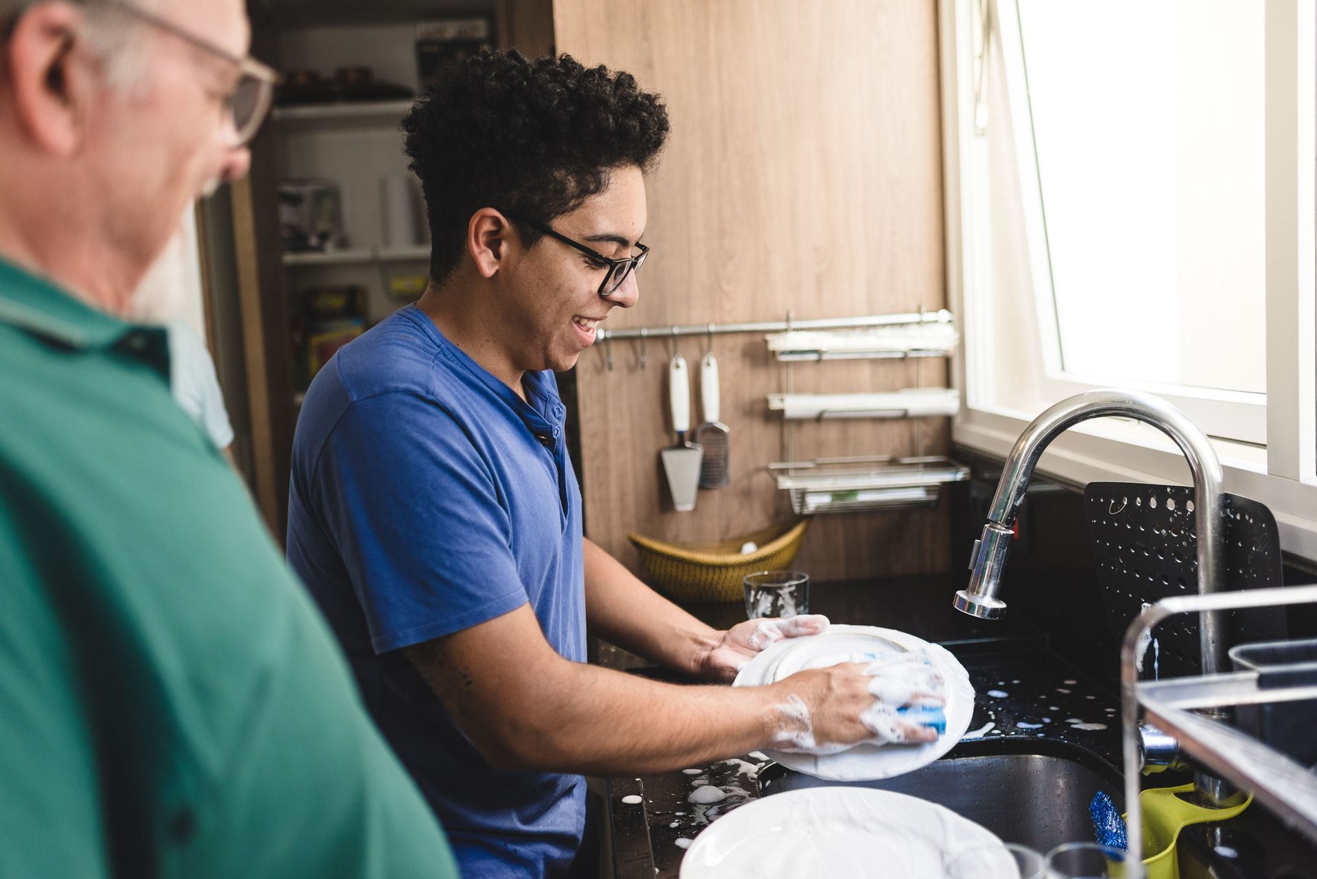 A man is washing dishes in a kitchen while talking to another man.