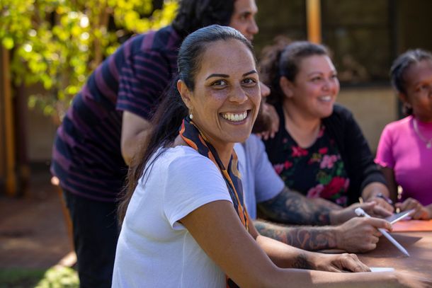A woman is smiling while sitting at a table with other people.