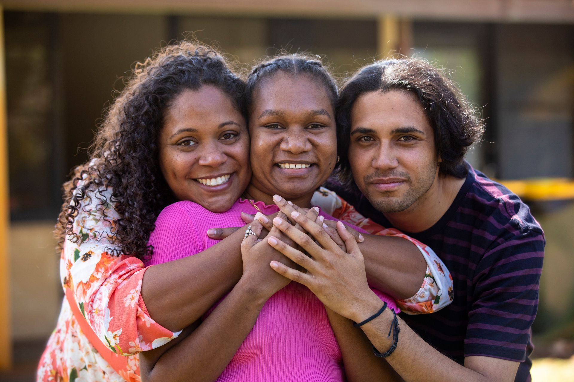 Three people are hugging each other and smiling for the camera.