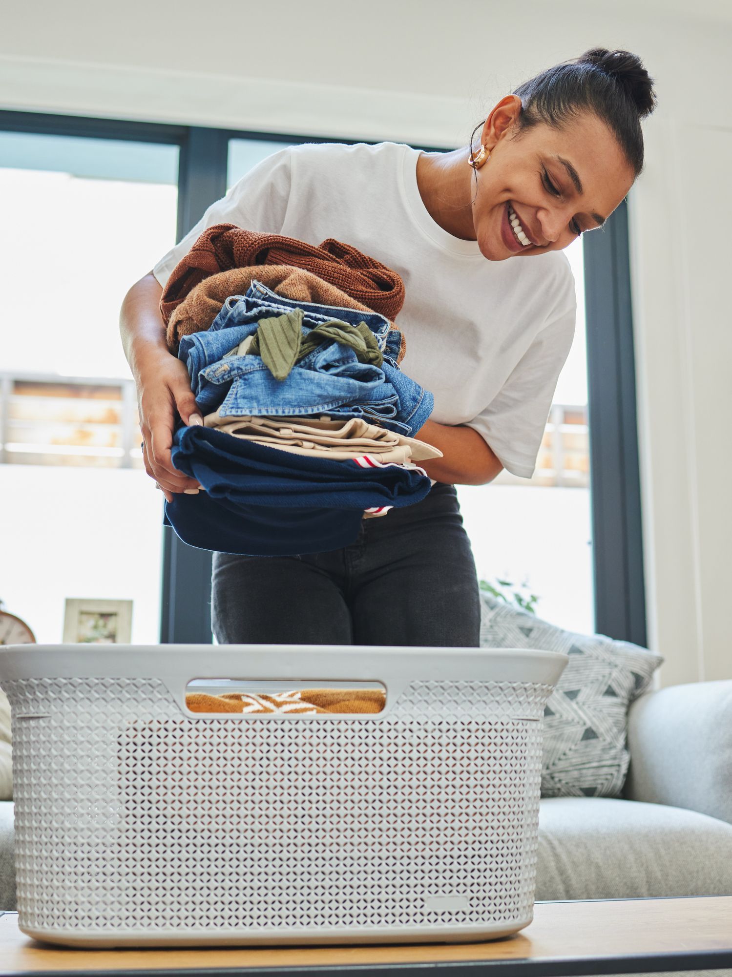 A woman is putting clothes in a laundry basket.