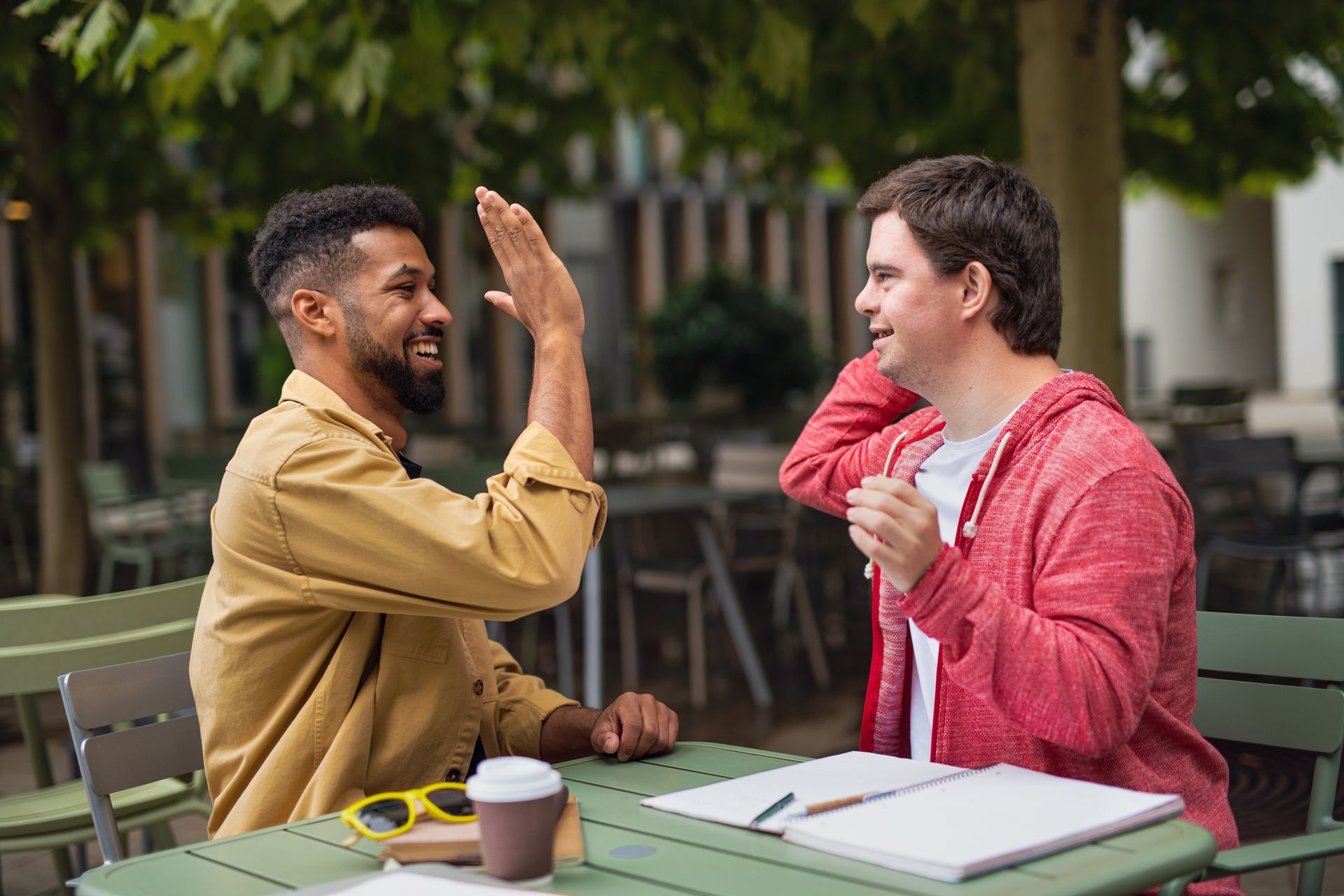 Two men are sitting at a table giving each other a high five.