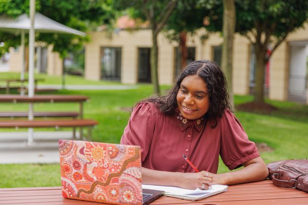 A woman is sitting at a table with a laptop and a notebook.