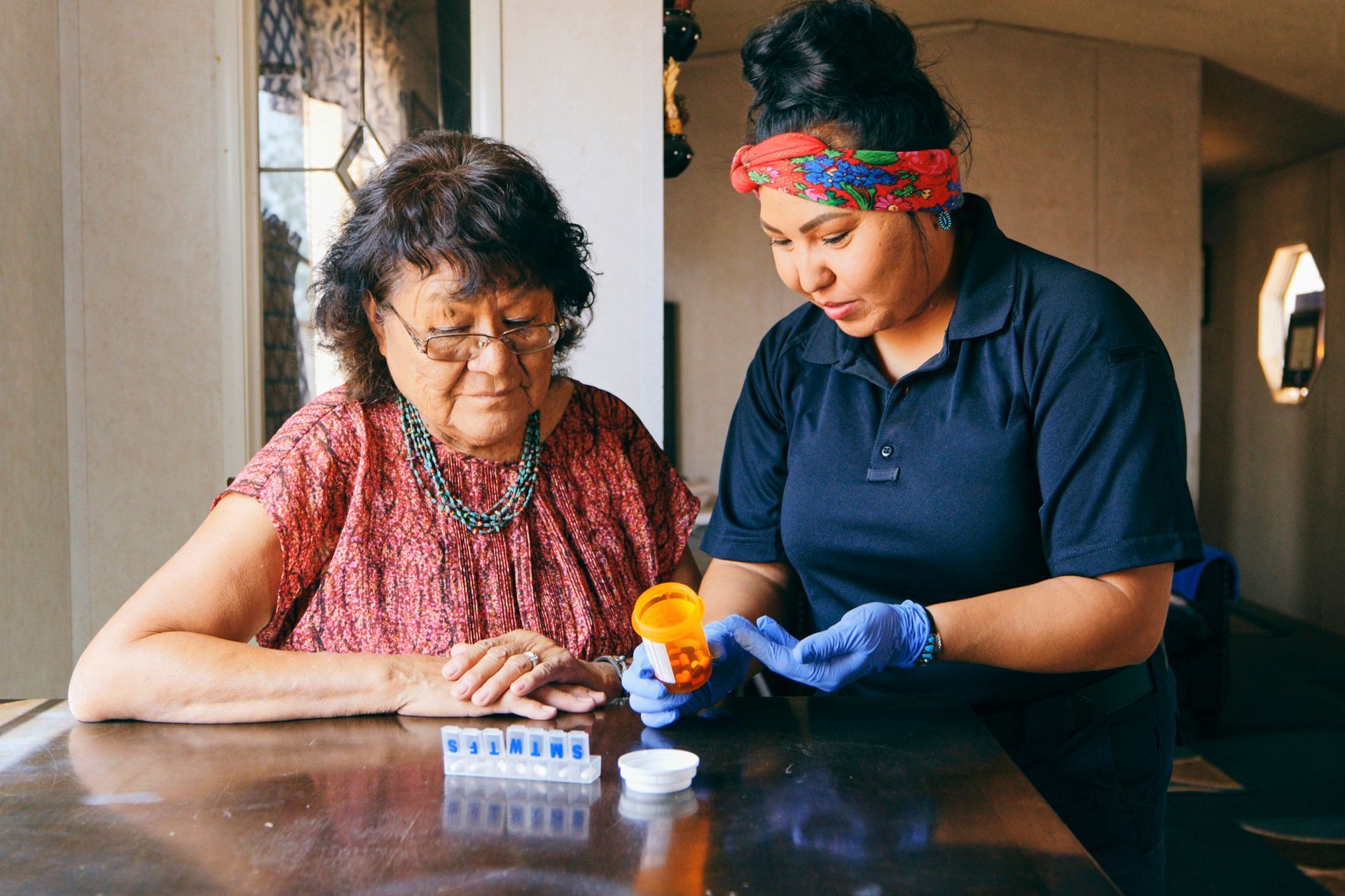 A young woman is helping an older woman with her medication.
