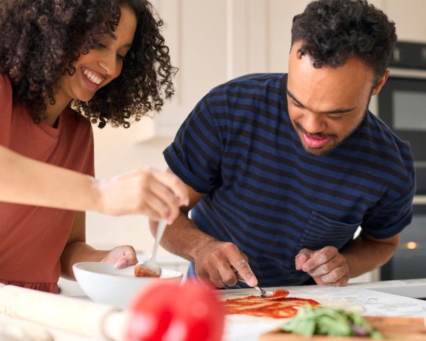 A man and a woman are making a pizza together in the kitchen.