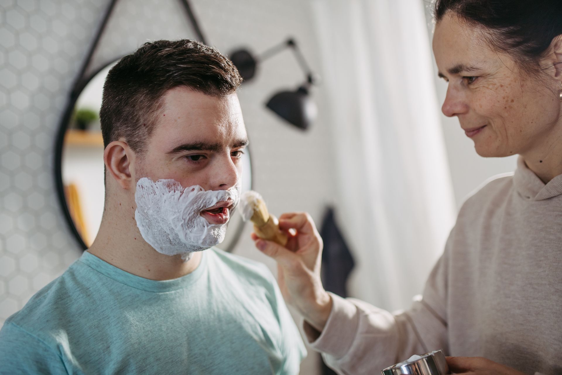 A woman is shaving a man's face in a bathroom.