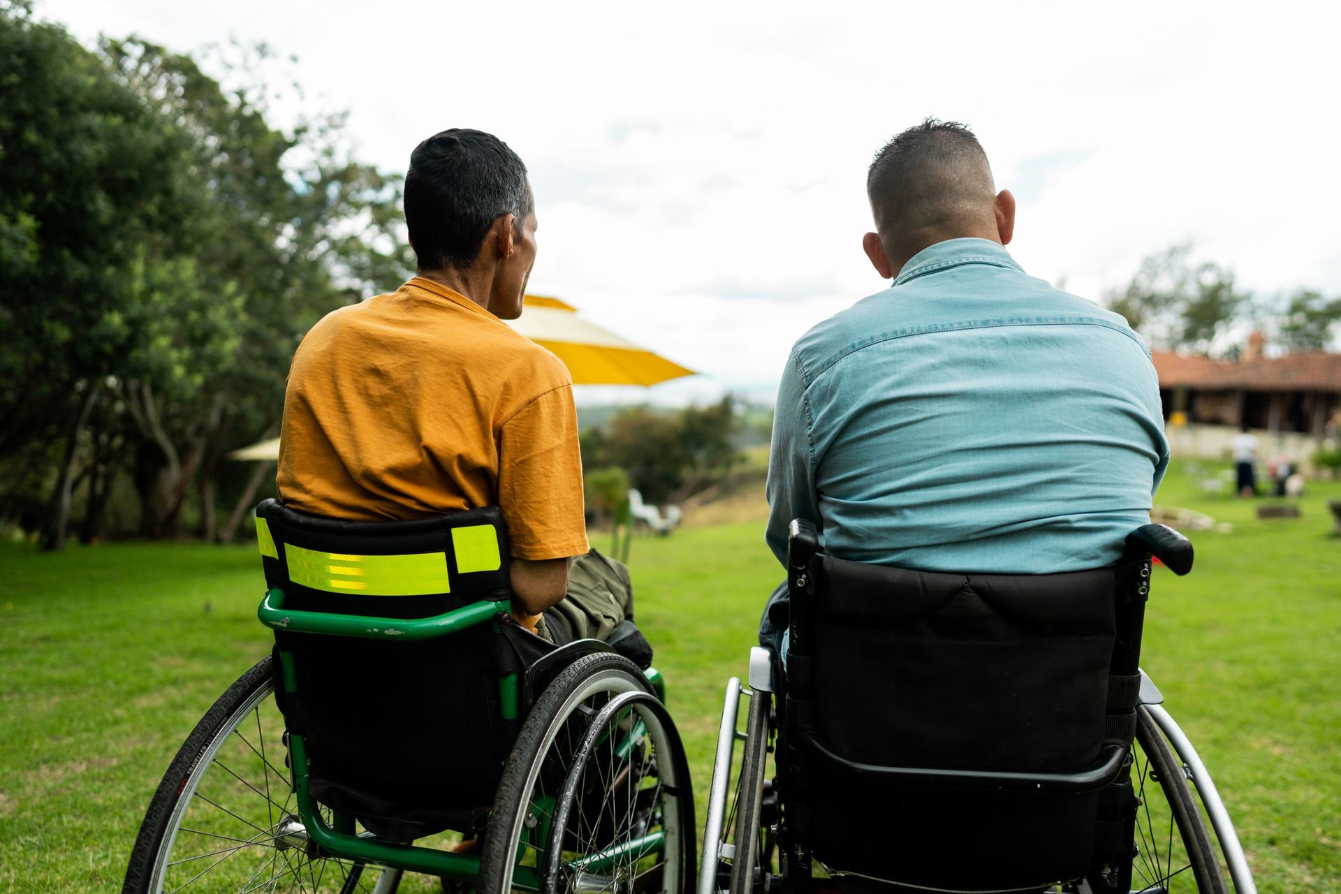 Two men in wheelchairs are sitting next to each other in a grassy field.