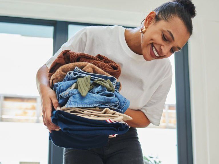 A woman is holding a pile of clothes and smiling.