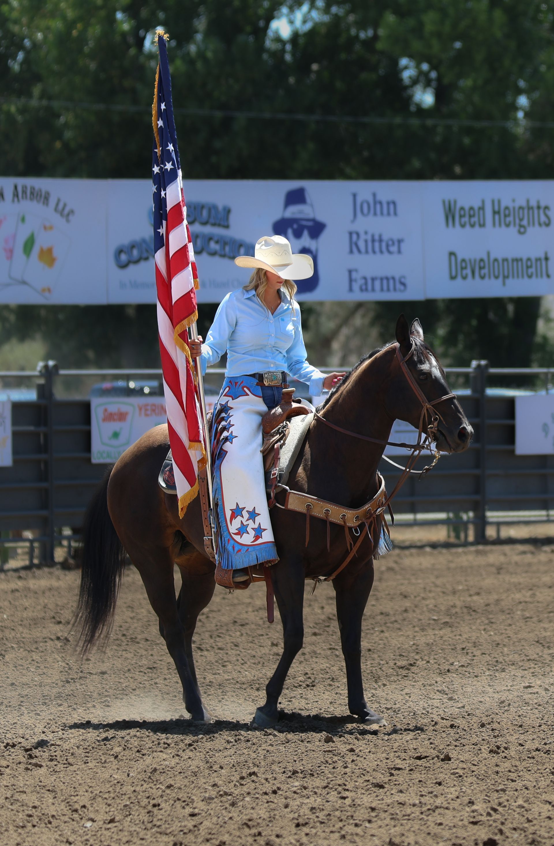 Cowgirl on horse carrying American flag in rodeo arena.