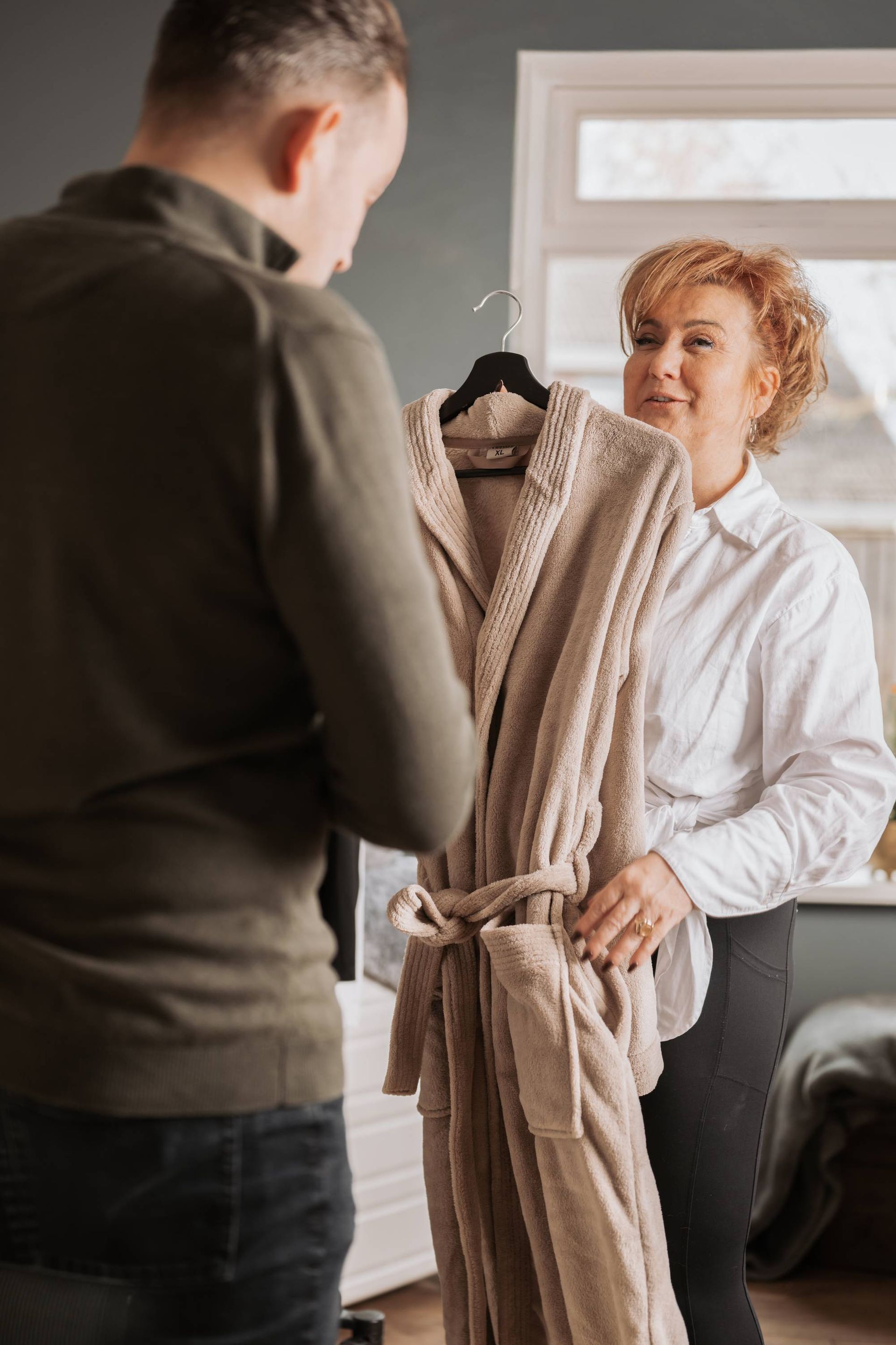 Vrouw met rood haar die aan de telefoon praat, zittend aan een houten tafel bij een raam.