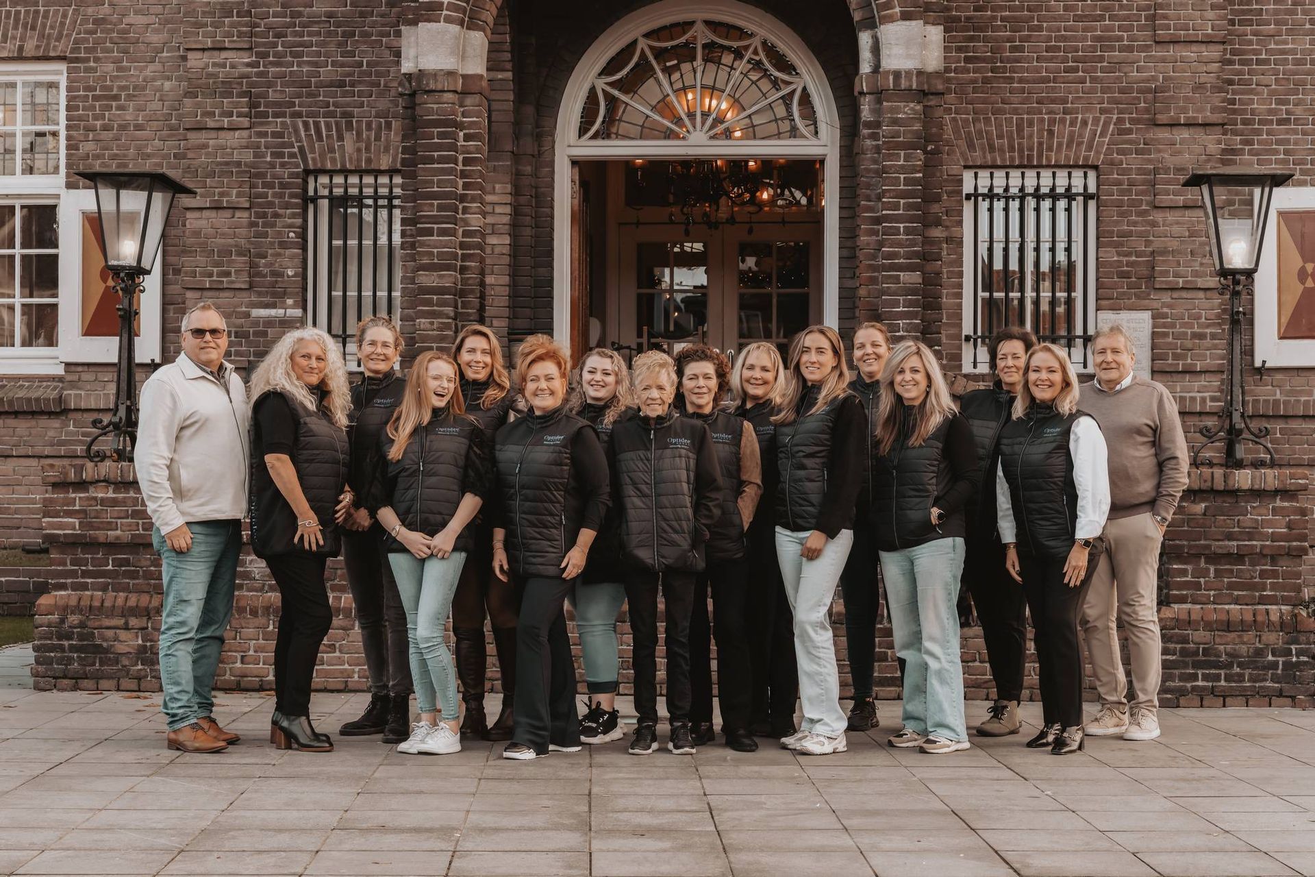 Een groep mensen poseert voor de ingang van een bakstenen gebouw. ​​Sommigen dragen hesjes. 