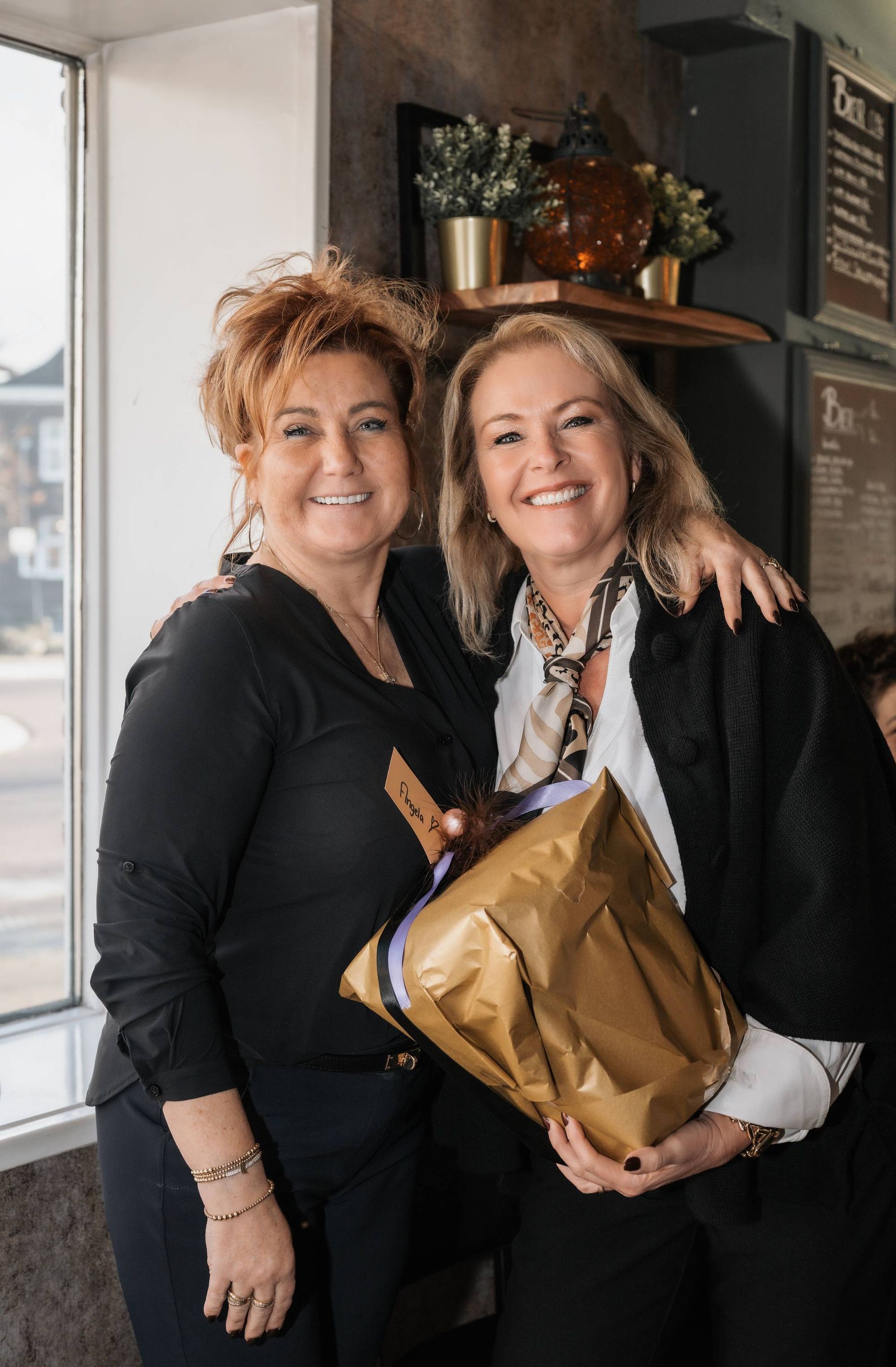 Een groep mensen poseert voor de ingang van een bakstenen gebouw. Ze dragen zwarte vesten en spijkerbroeken.