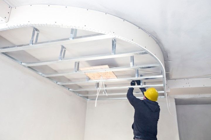 Worker in yellow hard hat installing ceiling framing in a white room