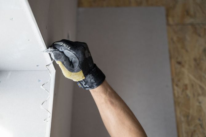 Gloved hand applying drywall tape or compound to a wall corner with a putty knife