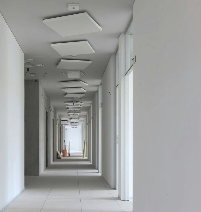 Long, empty white hallway with recessed ceiling lights and doors along the right wall